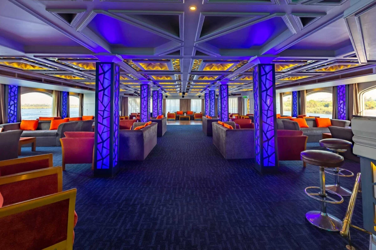 The lounge on the Solaris I Nile cruise lit in blue and purple, banquettes along both sides and a bar at the near end