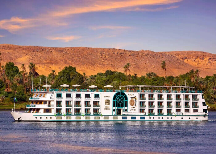 The Sonesta Moon Goddess Nile cruise ship on the Nile at dusk below a rocky escarpment