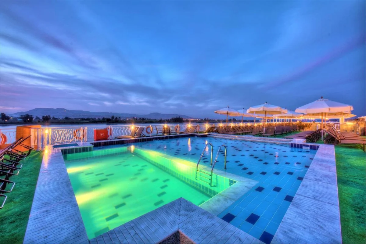 The lit swimming pool on the Steigenberger Legacy Nile cruise sun deck at dusk, parasols folded along the rail