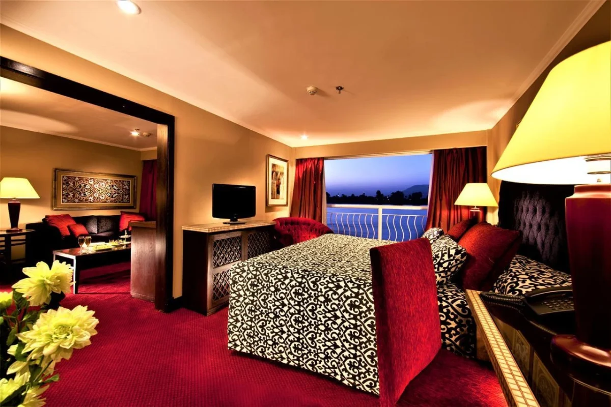 A suite on the Steigenberger Legacy Nile cruise with a patterned bedspread, red carpet and a window onto the Nile