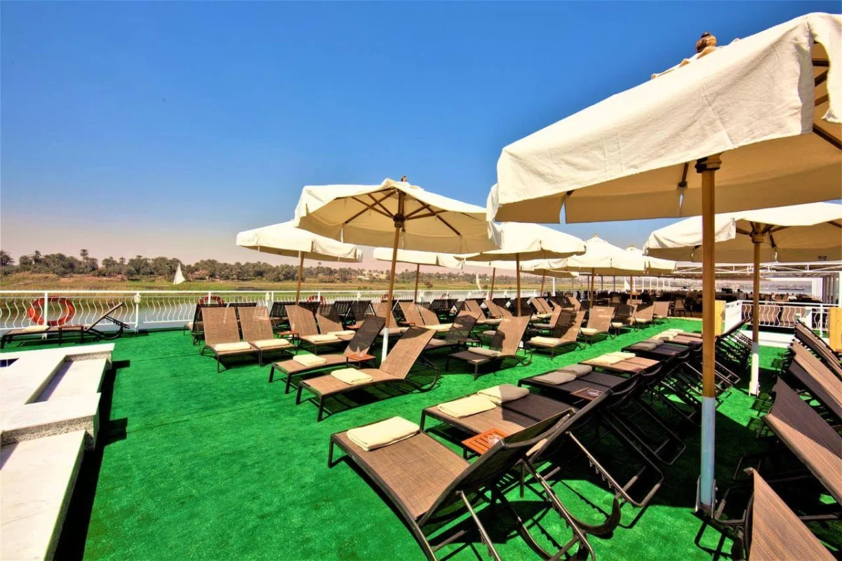 Loungers and white parasols on the Steigenberger Legacy Nile cruise sun deck, the riverbank green beyond