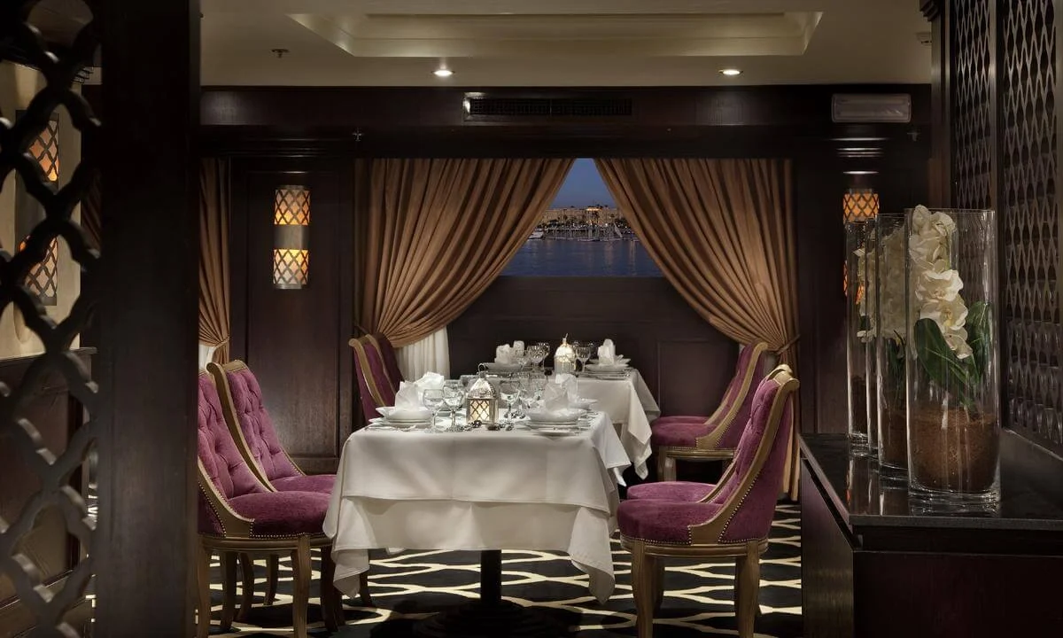 A table for two set in a curtained alcove on the Steigenberger Minerva Nile cruise, the river through the window behind