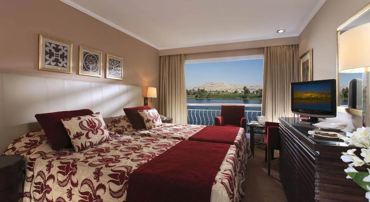 A twin-bed cabin on the Steigenberger Minerva Nile cruise with patterned covers and a wide window onto the Nile