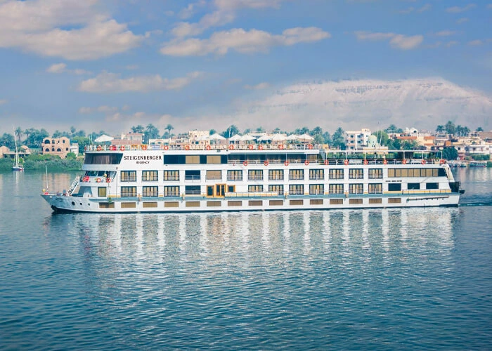 The Steigenberger Regency Nile cruise ship on the Nile with palms on the bank and the pale Theban hills behind