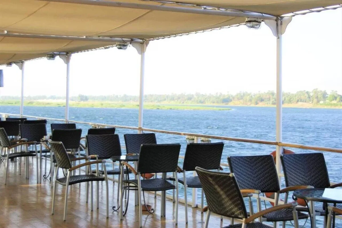 Chairs and tables under the deck canopy of the Steigenberger Royale Nile cruise, green fields along the far bank