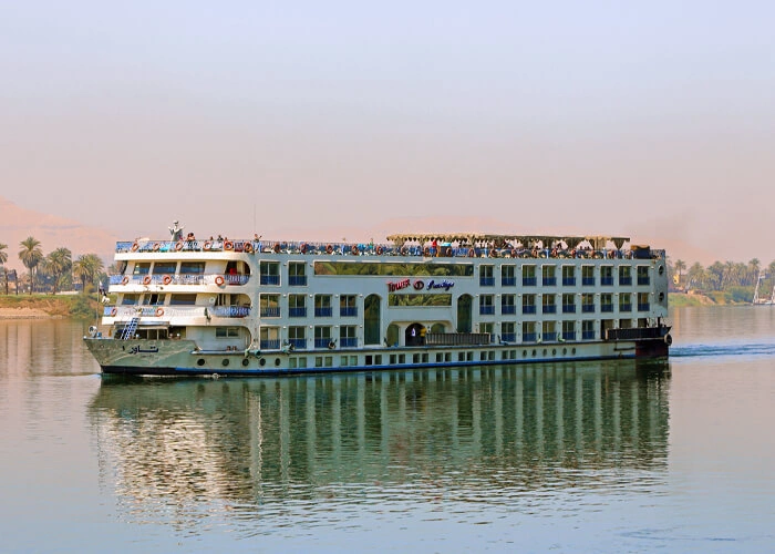 The Tower Prestige Nile cruise ship on the Nile, guests along the sun deck and trees on the bank behind