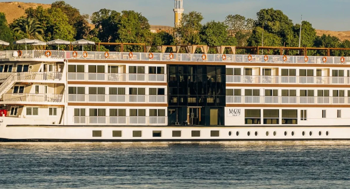 The Tulip Nile cruise ship seen broadside at its mooring, palms and desert hills rising behind the river