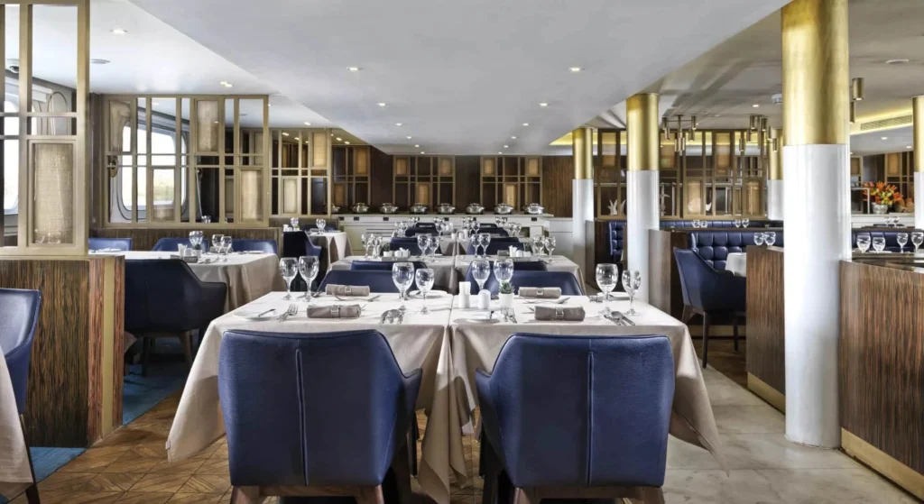 The restaurant on the Tulip Nile cruise, tables laid for dinner with navy leather chairs and gold-trimmed columns