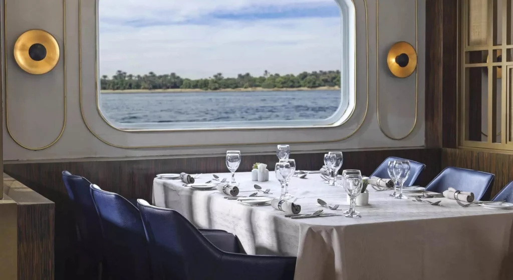 A restaurant table on the Tulip Nile cruise set with white linen and glassware beside a wide window looking out over the Nile
