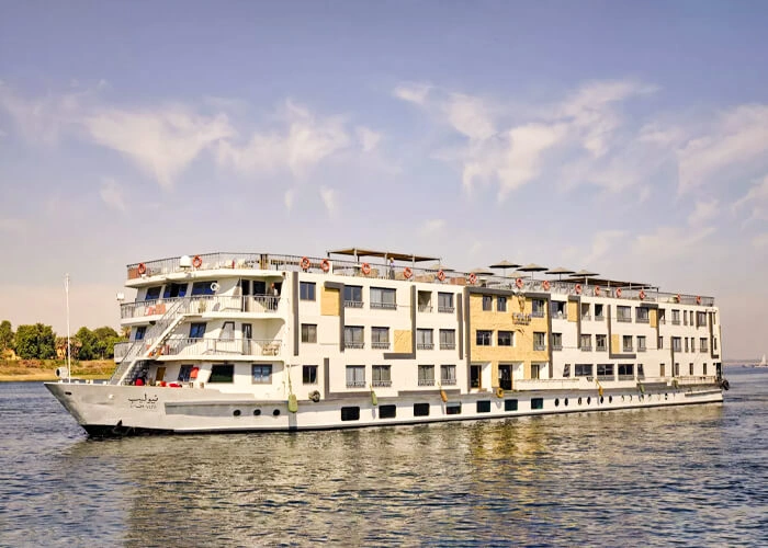 The Tulip Nile cruise ship sailing the Nile, its cream and white decks stacked four storeys above the water with a green riverbank behind